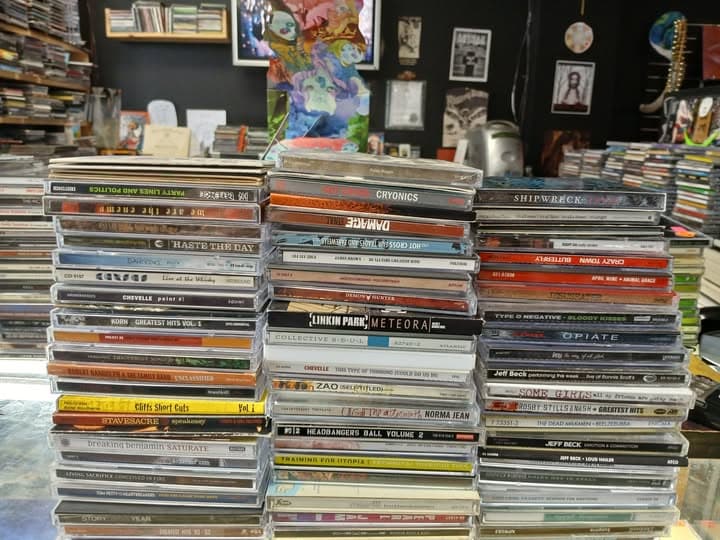 Three tall stacks of jewel-case CDs on the counter with wall art behind