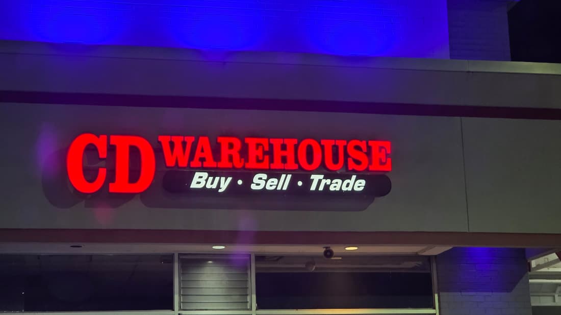 The illuminated CD Warehouse storefront sign at night.