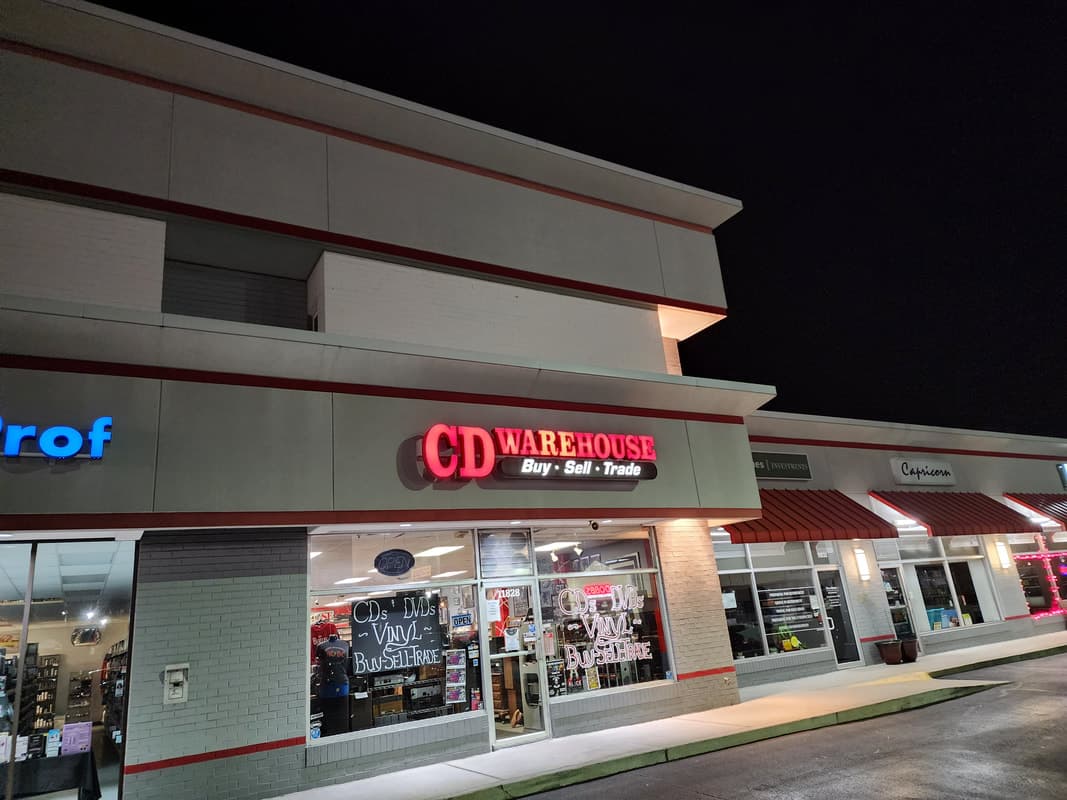 CD Warehouse storefront lit at night, full facade with illuminated sign and window displays