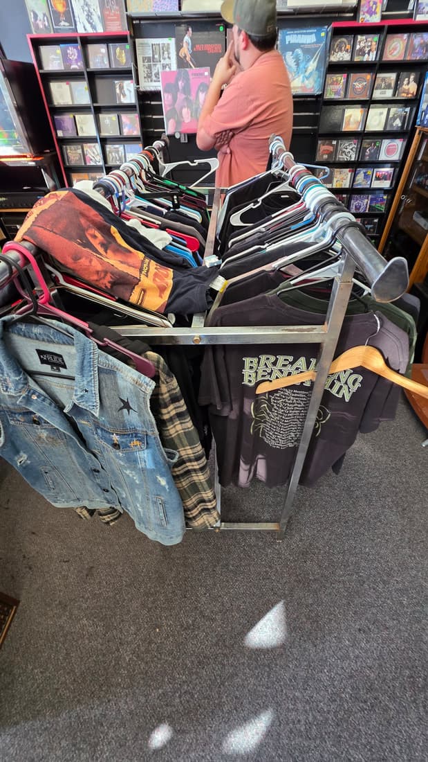 Customer browsing a rack of band tees and denim vests including Breaking Benjamin and Led Zeppelin