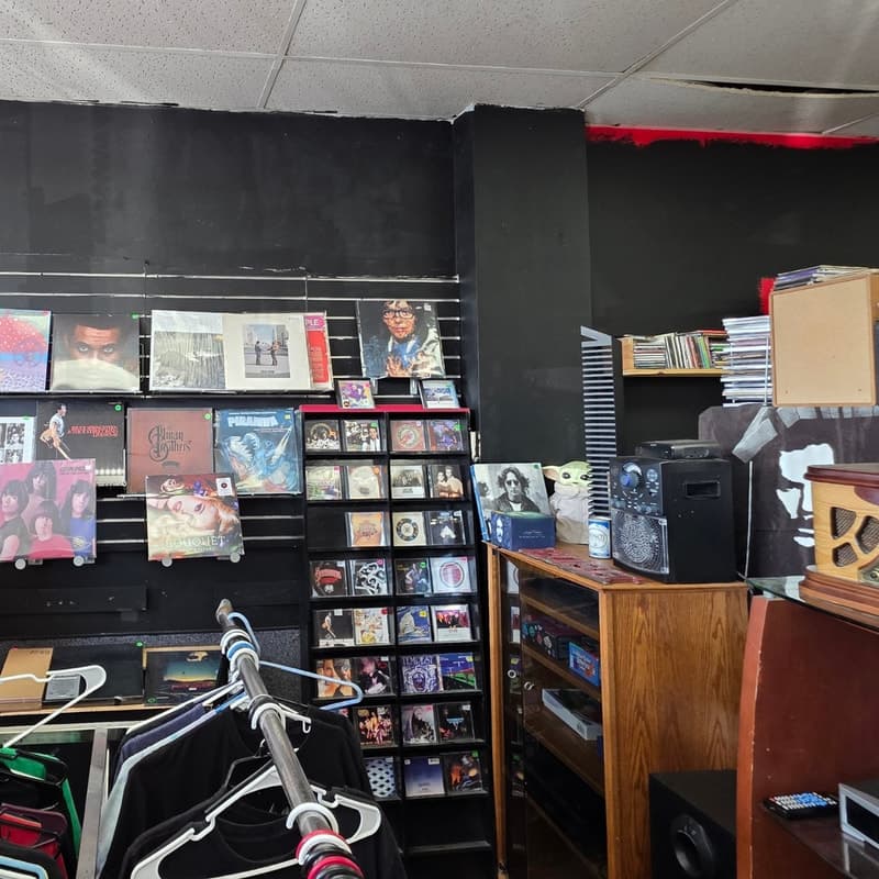 Rack of vintage band tees and denim beside vinyl crates and stereo components