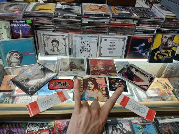 A hand throwing devil horns over the CD counter display, Rage Against the Machine and 311 discs visible