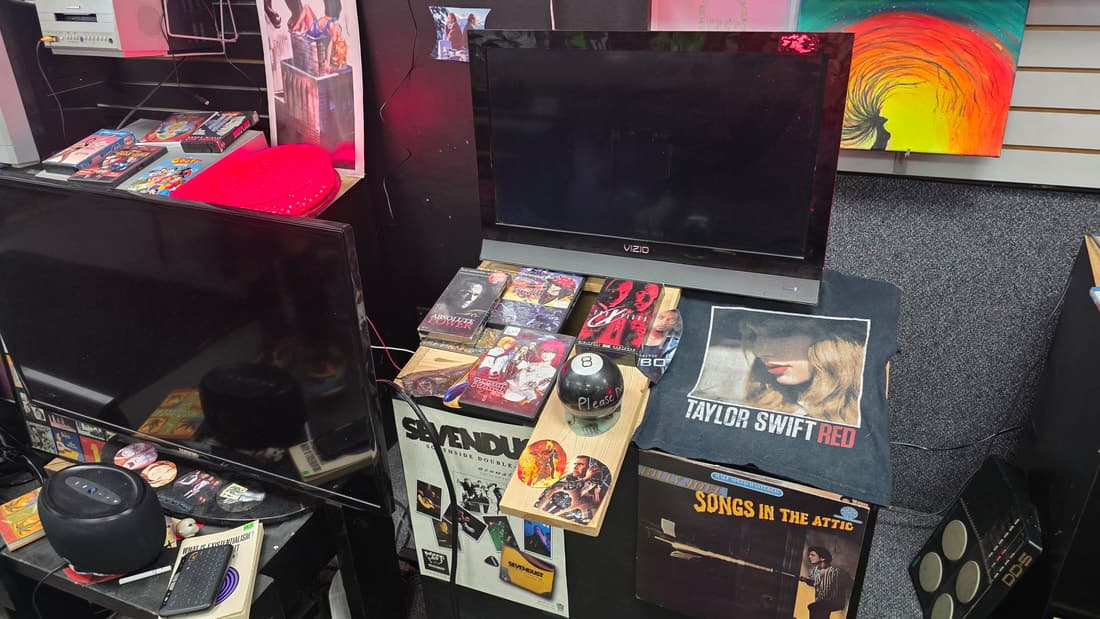 Wider view of the oddities shelf with a VIZIO TV, band tee, Sevendust poster and Magic 8-Ball
