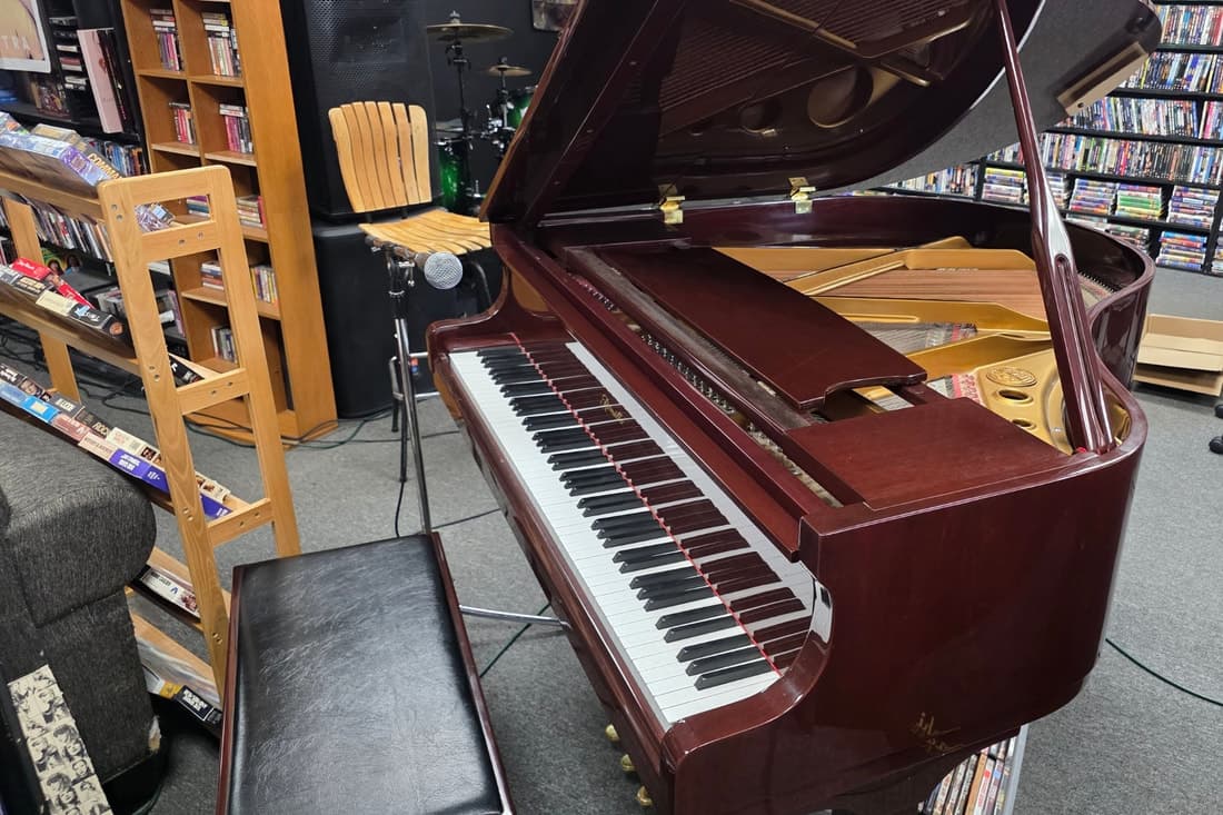 A mahogany grand piano with its lid open and a mic stand beside it, DVD shelving all around.