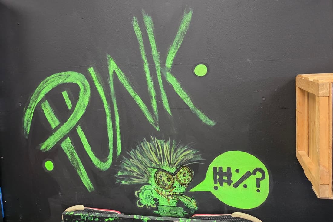 Green chalk PUNK mural with a spiky-haired cartoon character on the black wall above a skate deck