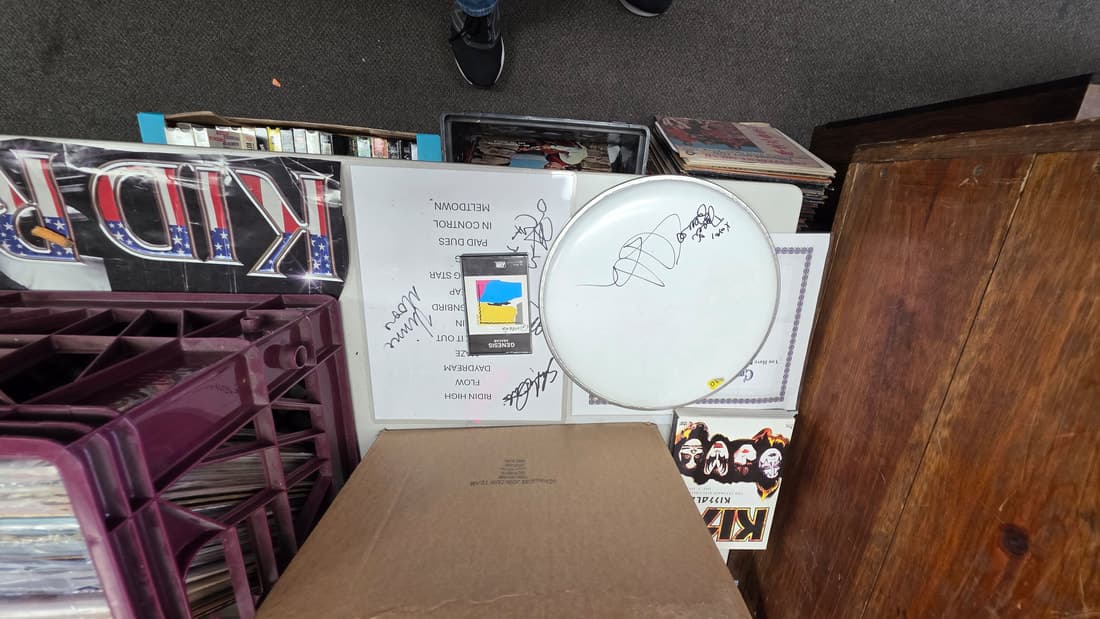 Signed drumhead and a KISS poster above milk crates of vinyl