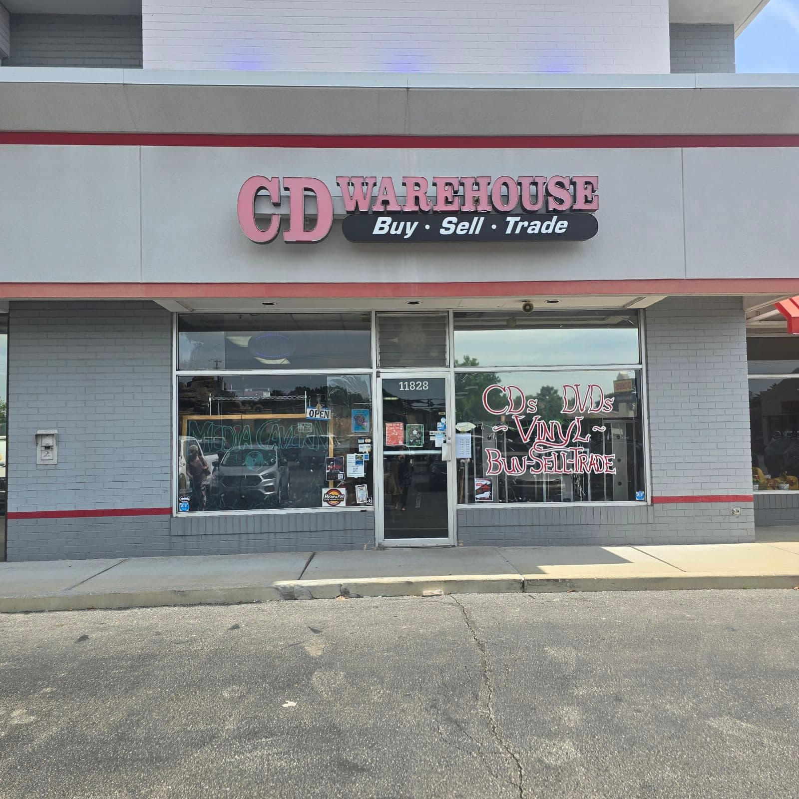 The storefront at 11828 in daylight: CD Warehouse signage still on the facade, MEDIA CAVERN lettered in the window glass.