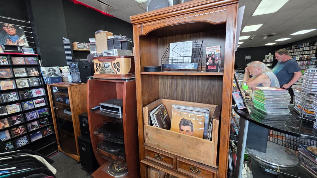Vintage stereo console and turntable in a wooden hutch stacked with LPs, two customers at the counter behind